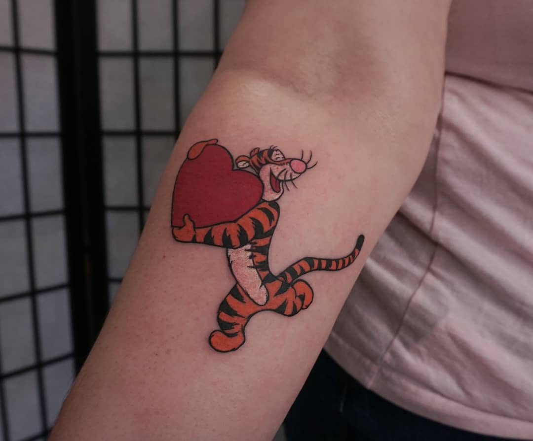 Tattoo of Tigger holding a red heart on an arm
